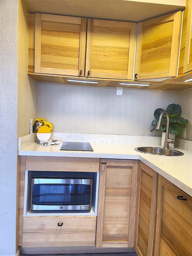 kitchen featuring light countertops, a textured wall, stainless steel microwave, and a sink