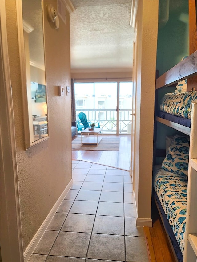 corridor featuring a textured wall, baseboards, a textured ceiling, and tile patterned floors