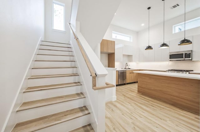 staircase with a wealth of natural light, wood finished floors, visible vents, and baseboards