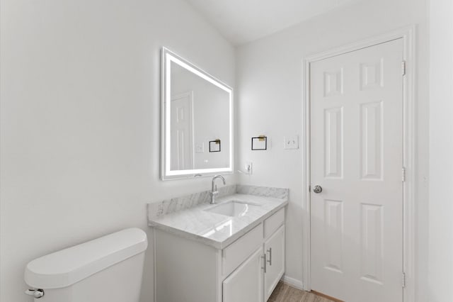 half bath featuring wood finished floors, toilet, and vanity