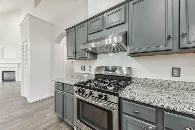 kitchen with stainless steel gas range, arched walkways, light wood-style flooring, light stone countertops, and ventilation hood