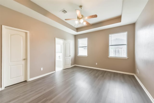 unfurnished bedroom featuring a tray ceiling, dark wood finished floors, baseboards, visible vents, and ensuite bath