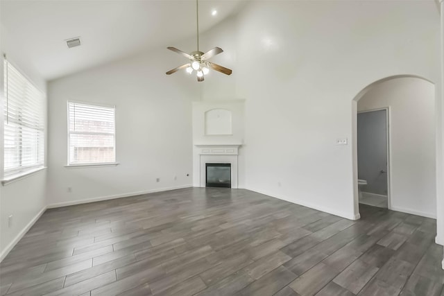 unfurnished living room with a ceiling fan, a glass covered fireplace, arched walkways, visible vents, and dark wood-style floors