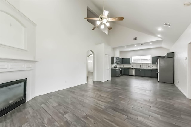unfurnished living room featuring visible vents, a ceiling fan, a glass covered fireplace, high vaulted ceiling, and dark wood-style flooring