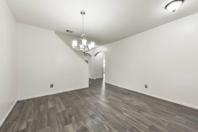 unfurnished dining area with a notable chandelier, baseboards, arched walkways, and dark wood-type flooring