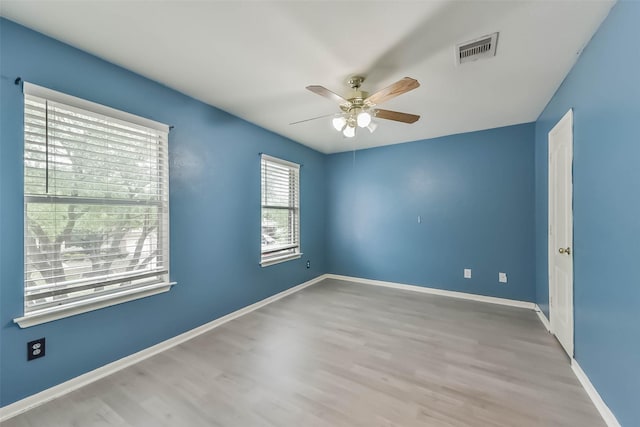spare room featuring wood finished floors, visible vents, baseboards, and ceiling fan