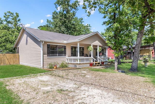 ranch-style house with fence, a porch, a shingled roof, and a front yard