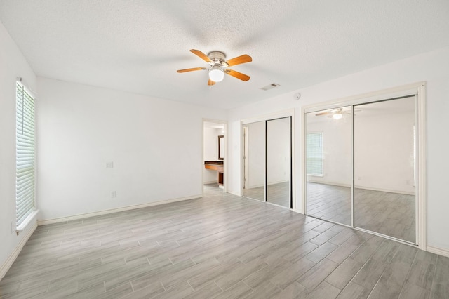 1823 Mandrill Ln, Houston, TX 77067 - unfurnished bedroom with light wood-style floors, a textured ceiling, baseboards, and two closets