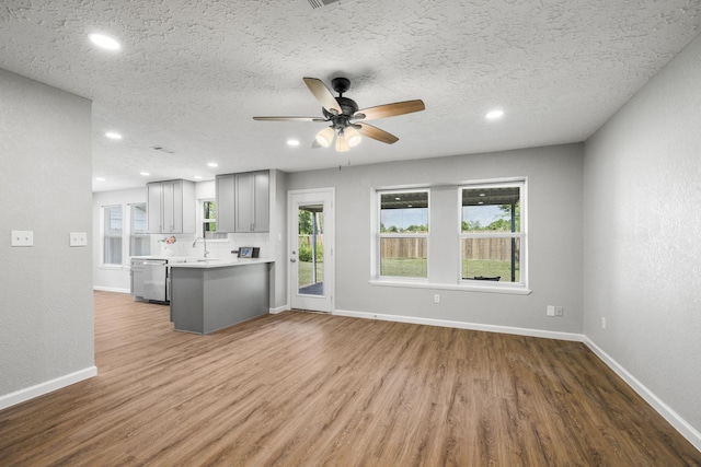 kitchen with light countertops, wood finished floors, stainless steel dishwasher, and gray cabinetry