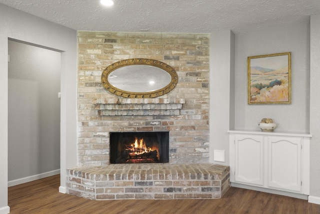 room details with baseboards, wood finished floors, a brick fireplace, and a textured ceiling