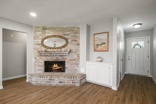 living room featuring a brick fireplace, wood finished floors, a textured ceiling, and baseboards