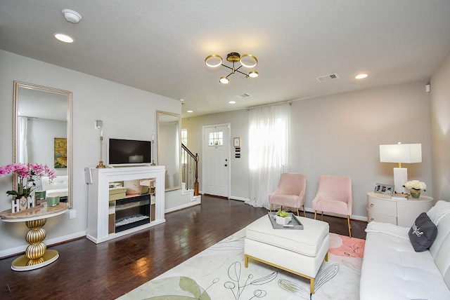 living room featuring baseboards, visible vents, a chandelier, wood finished floors, and stairway