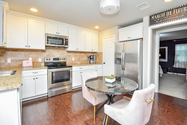 kitchen featuring white cabinets, dark wood-style floors, stainless steel appliances, light stone counters, and tasteful backsplash
