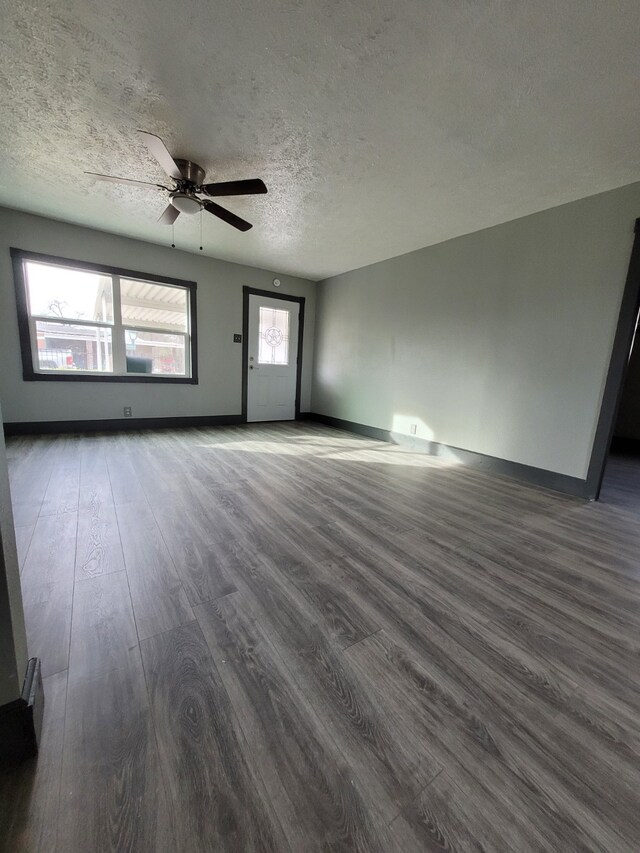 unfurnished living room with baseboards, a textured ceiling, dark wood-style floors, and ceiling fan