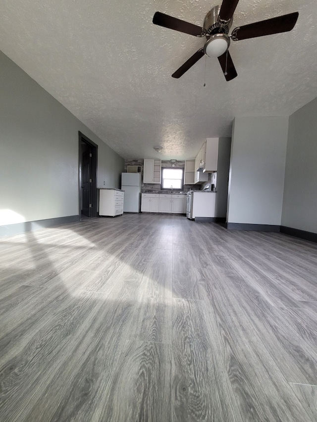 unfurnished living room with baseboards, a ceiling fan, wood finished floors, and a textured ceiling