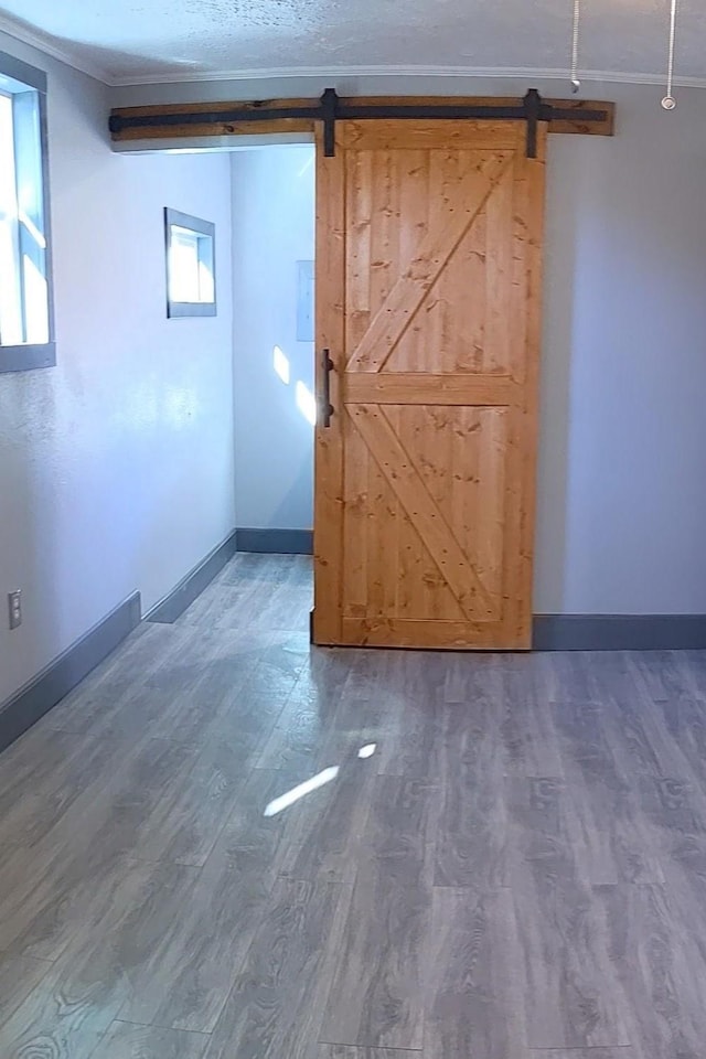 interior space featuring a barn door, wood finished floors, crown molding, and baseboards