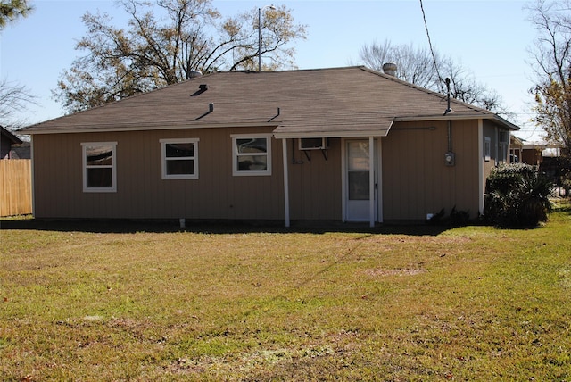 back of house with a lawn, fence, and roof with shingles