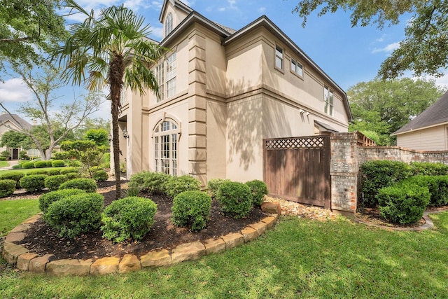 view of property exterior featuring fence, stucco siding, and a lawn