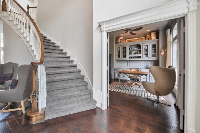 staircase featuring wood-type flooring, a ceiling fan, and baseboards