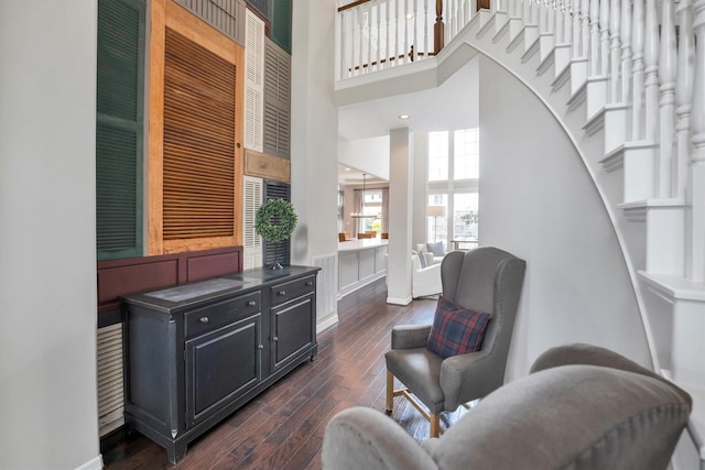 sitting room featuring dark wood finished floors, stairway, baseboards, and a towering ceiling