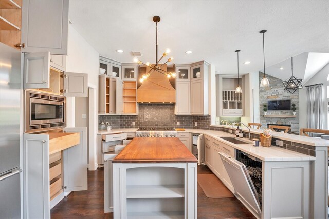 kitchen with a sink, stainless steel appliances, open shelves, a peninsula, and butcher block counters