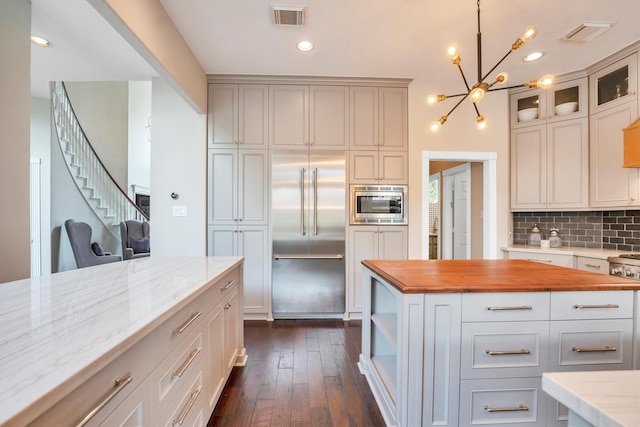 kitchen with an inviting chandelier, decorative backsplash, butcher block counters, built in appliances, and visible vents