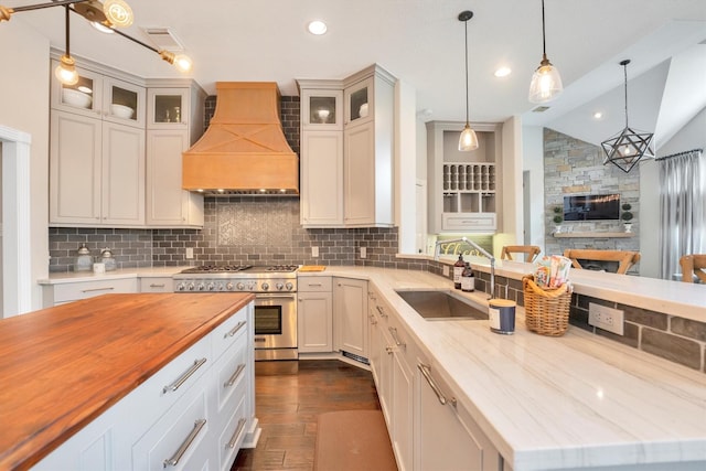 kitchen with dark wood-style flooring, custom range hood, stainless steel range, backsplash, and butcher block counters