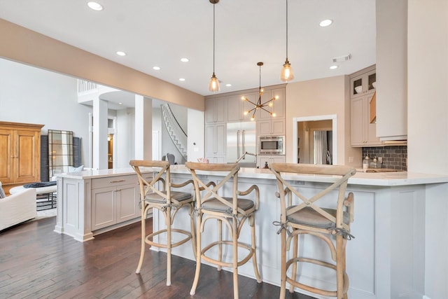 kitchen with stainless steel microwave, dark wood-style flooring, a peninsula, backsplash, and light countertops