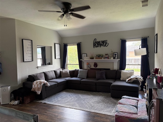 living room with a textured ceiling, visible vents, vaulted ceiling, wood finished floors, and a ceiling fan
