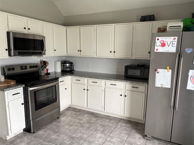kitchen with dark stone countertops, appliances with stainless steel finishes, backsplash, light tile patterned flooring, and lofted ceiling