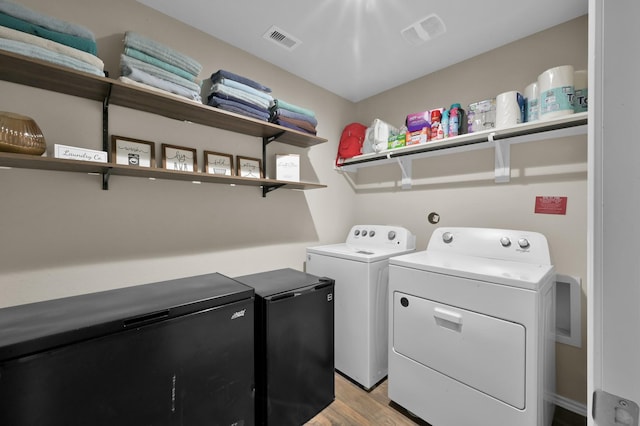 clothes washing area with light wood-type flooring, visible vents, washer and dryer, and laundry area