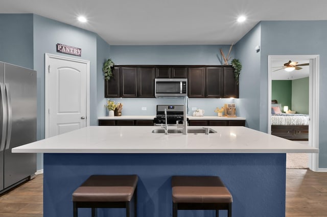 kitchen featuring a kitchen breakfast bar, a sink, wood finished floors, light countertops, and appliances with stainless steel finishes