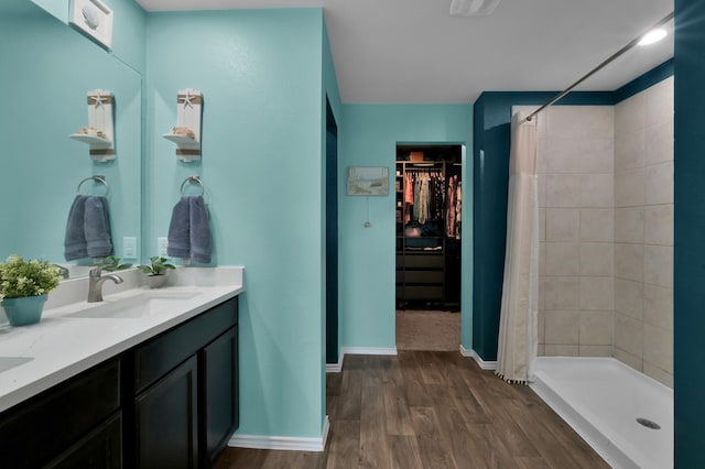 bathroom with wood finished floors, a sink, a stall shower, a walk in closet, and double vanity