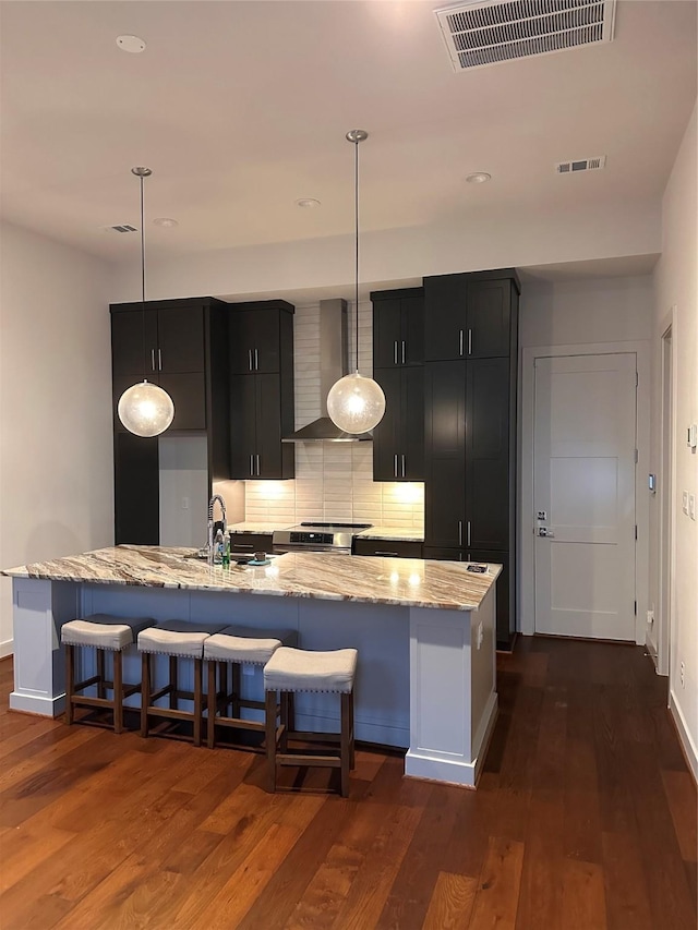 2409 Webster St, Houston, TX 77003 - kitchen featuring dark cabinets, a large island with sink, wall chimney exhaust hood, dark wood-style floors, and a breakfast bar