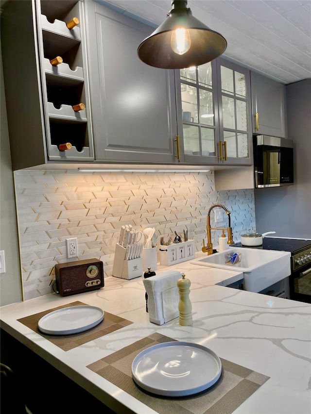 kitchen featuring decorative backsplash, light stone countertops, a sink, and glass insert cabinets