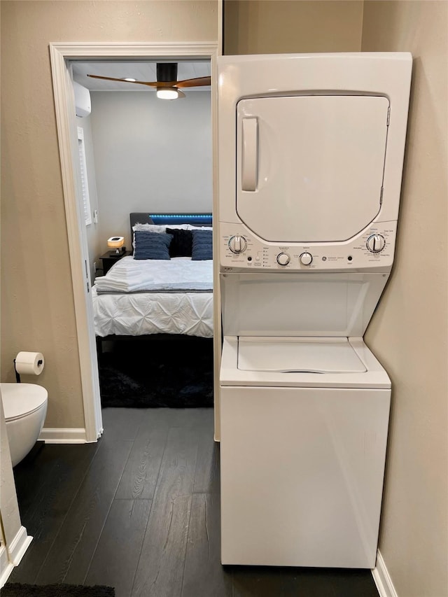 washroom featuring baseboards, a ceiling fan, stacked washer and clothes dryer, and dark wood-type flooring