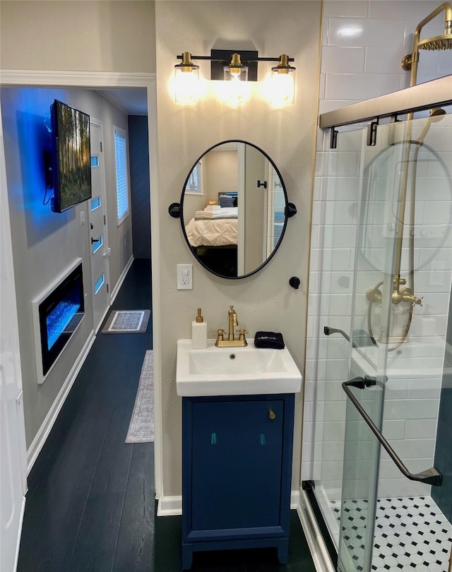 ensuite bathroom featuring a shower stall, wood finished floors, vanity, ensuite bath, and baseboards