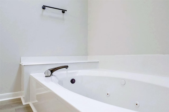 full bathroom with wood finished floors, a jetted tub, and baseboards
