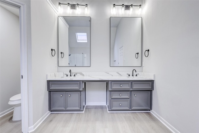 bathroom with baseboards, toilet, a sink, double vanity, and wood finished floors