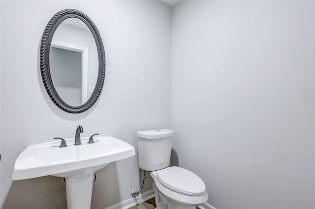 half bath with toilet, baseboards, and a sink