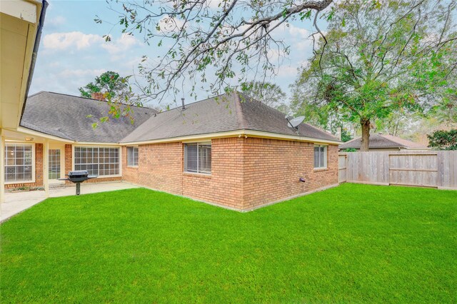 rear view of property featuring brick siding, a patio, a fenced backyard, a chimney, and a lawn