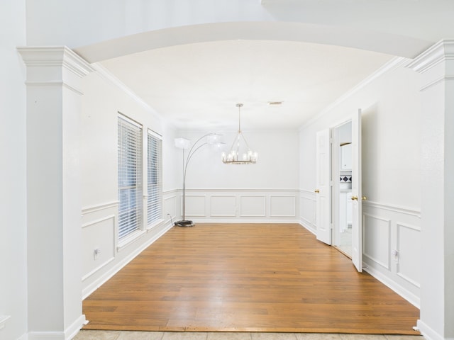 unfurnished dining area with a chandelier, light wood-style flooring, a decorative wall, and ornamental molding