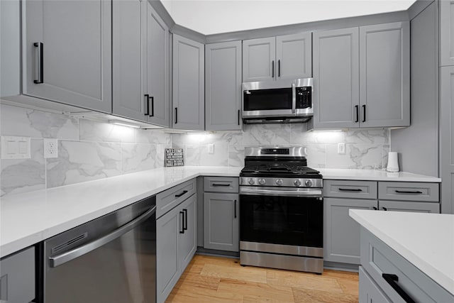 kitchen with gray cabinets, appliances with stainless steel finishes, tasteful backsplash, and light countertops