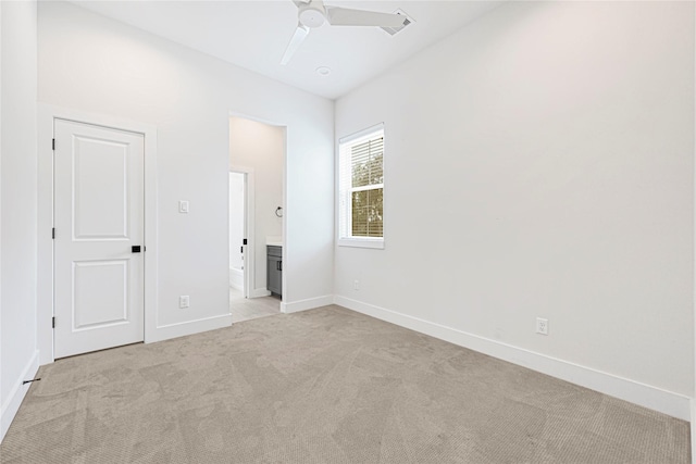 unfurnished bedroom featuring ceiling fan, ensuite bath, baseboards, and light colored carpet