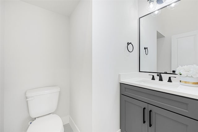 half bath with baseboards, vanity, and toilet