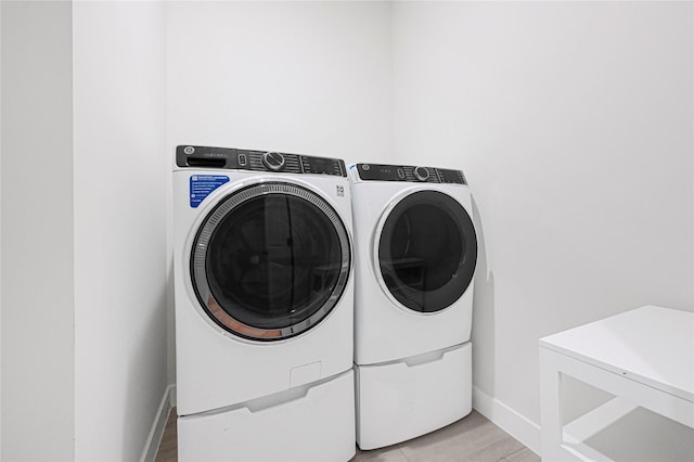 washroom with light wood-type flooring, washing machine and clothes dryer, baseboards, and laundry area