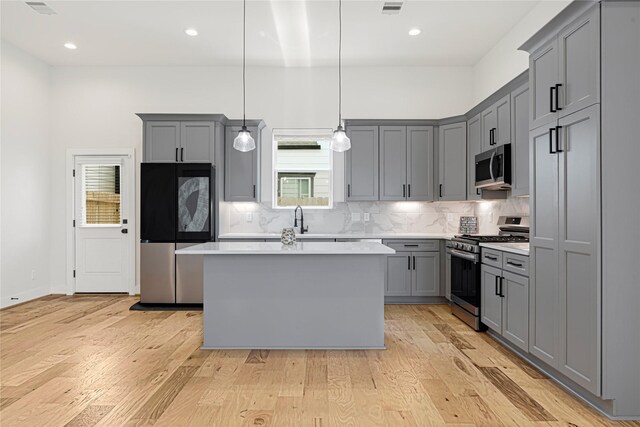 kitchen featuring tasteful backsplash, gray cabinets, stainless steel appliances, light countertops, and a kitchen island