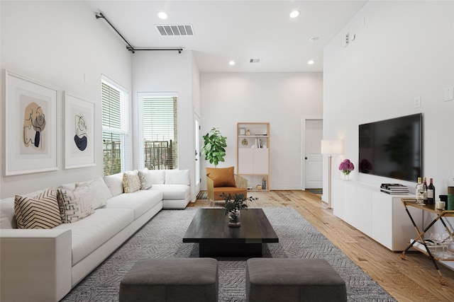 living room featuring recessed lighting, light wood-type flooring, visible vents, and a high ceiling