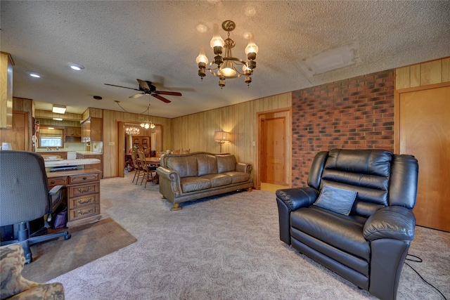 living area featuring a textured ceiling, wood walls, light carpet, and ceiling fan with notable chandelier