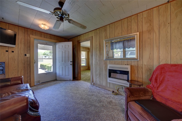 carpeted living area featuring heating unit, wood walls, a fireplace, and a ceiling fan